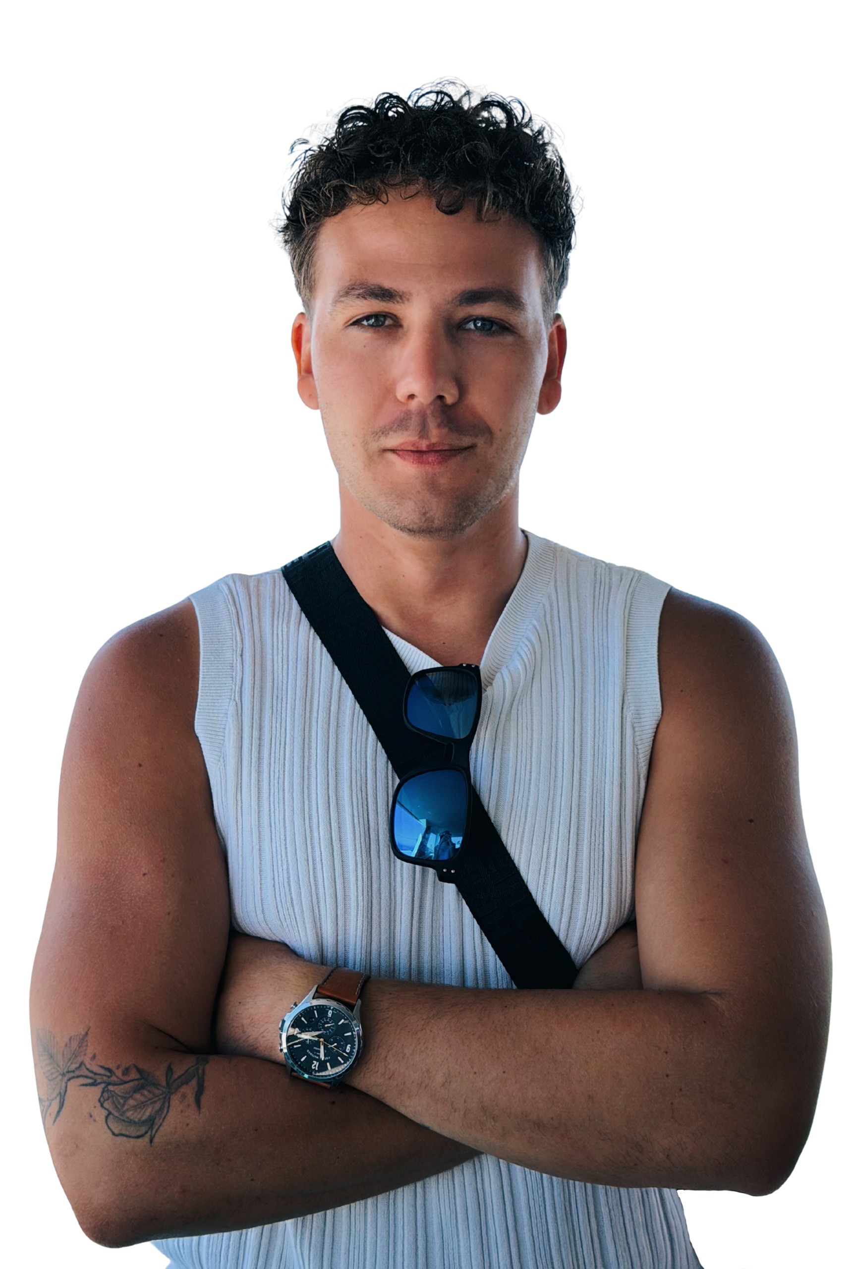 Portrait of a man with short curly hair wearing a sleeveless white top with arms crossed a watch on his wrist sunglasses hanging from a strap and a subtle forearm tattoo against a dark background